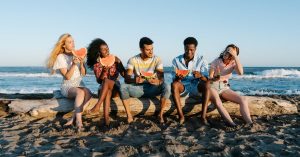 group of young smiling multiethnic partners eating delicious watermelon slices while sitting on fall